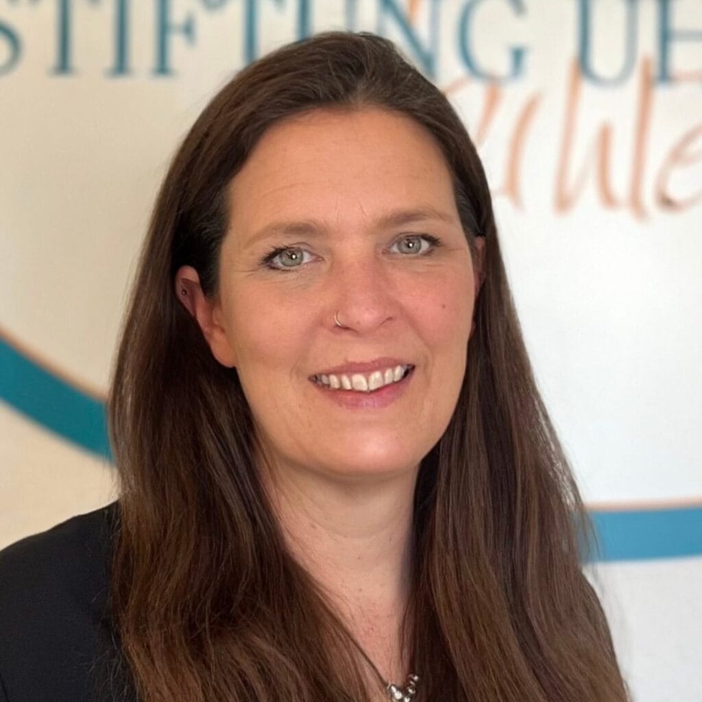 Tatjana Harrs lächelt in die Kamera. Sie hat dunkelbraune lange Haare und trägt ein dunkles Oberteil. Sie hat ein Nasenpiercing.