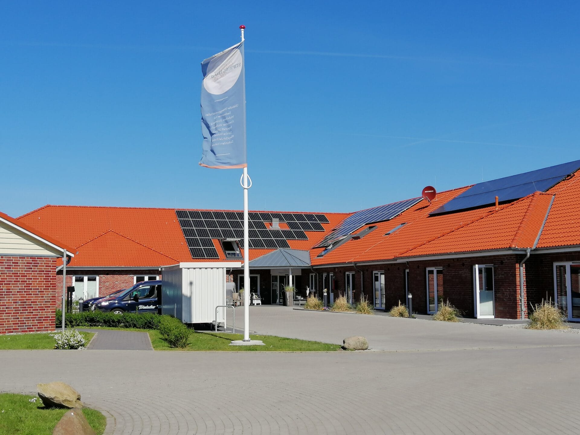 Das Gebäude mit Sicht auf den Eingangsbereich des Pflegezentrums Uhlebüll. Eine Firmenflagge weht im Vordergrund